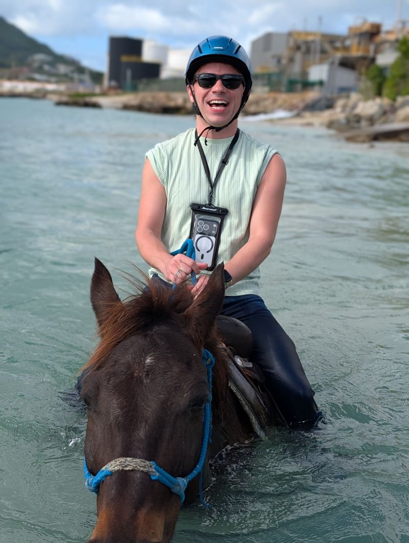 Justin laughing while riding a horse through the ocean in the Caribbean